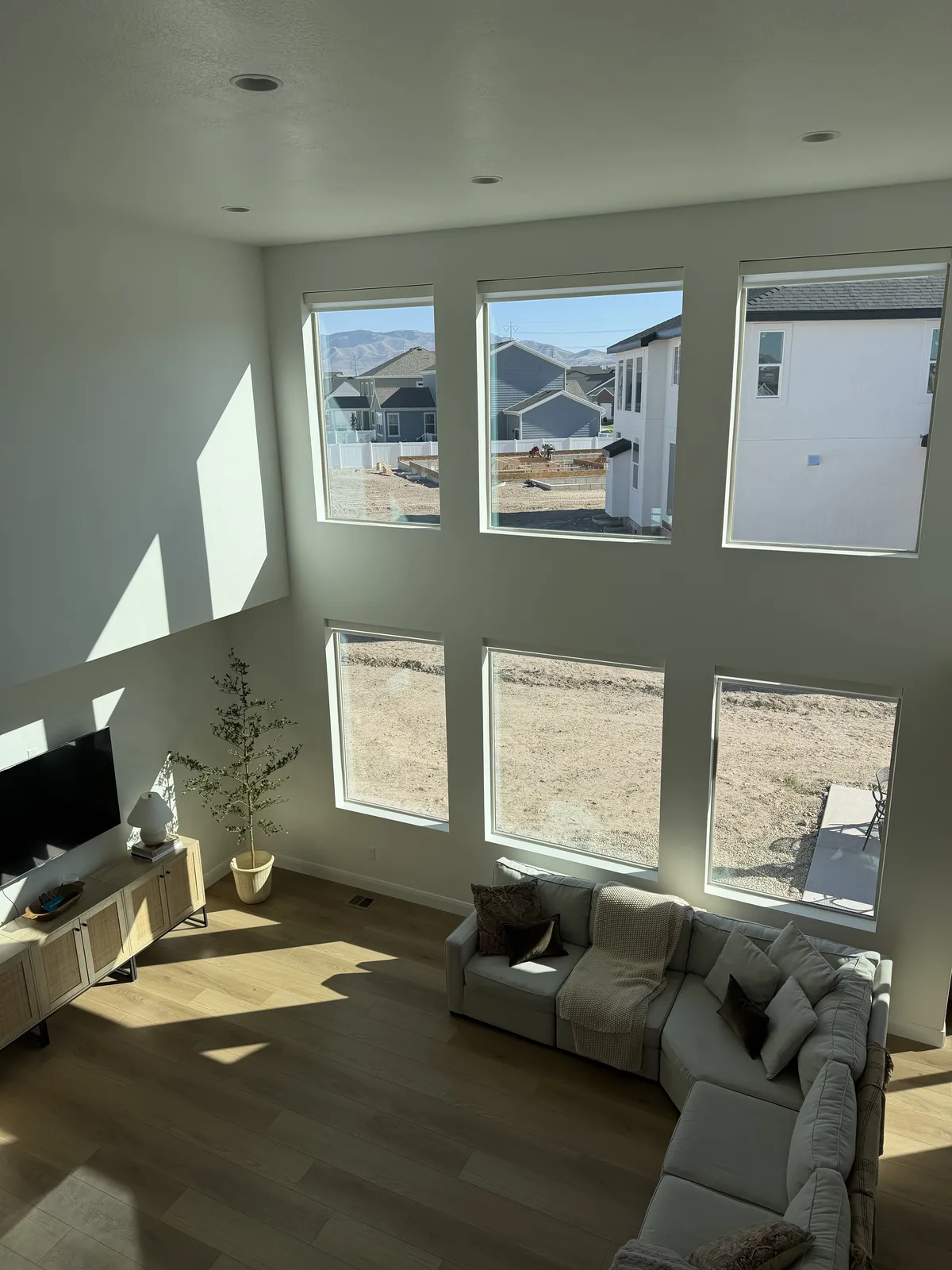 Two-story great room with a wall of tall windows fitted with motorized roller shades, sectional sofa in the foreground